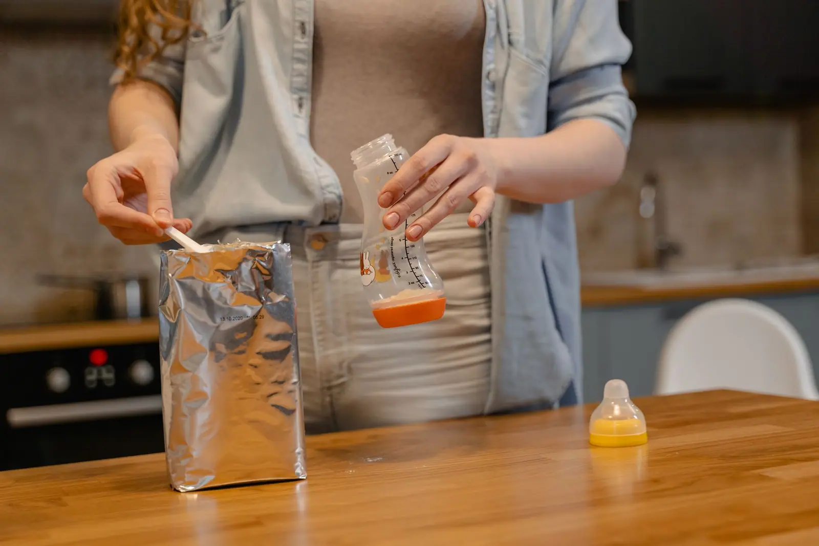 A person measuring powder at a kitchen counter with a baby bottle beside them