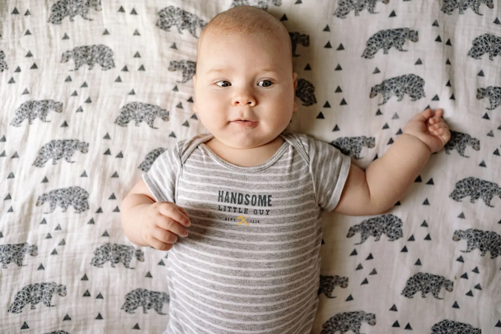 A baby lying on their back on a patterned crib sheet