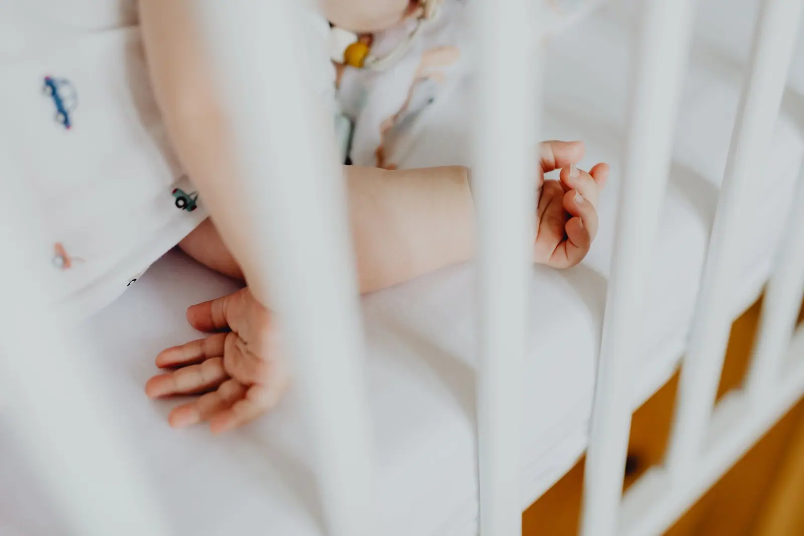 A baby's hands and feet visible through the white rails of a crib