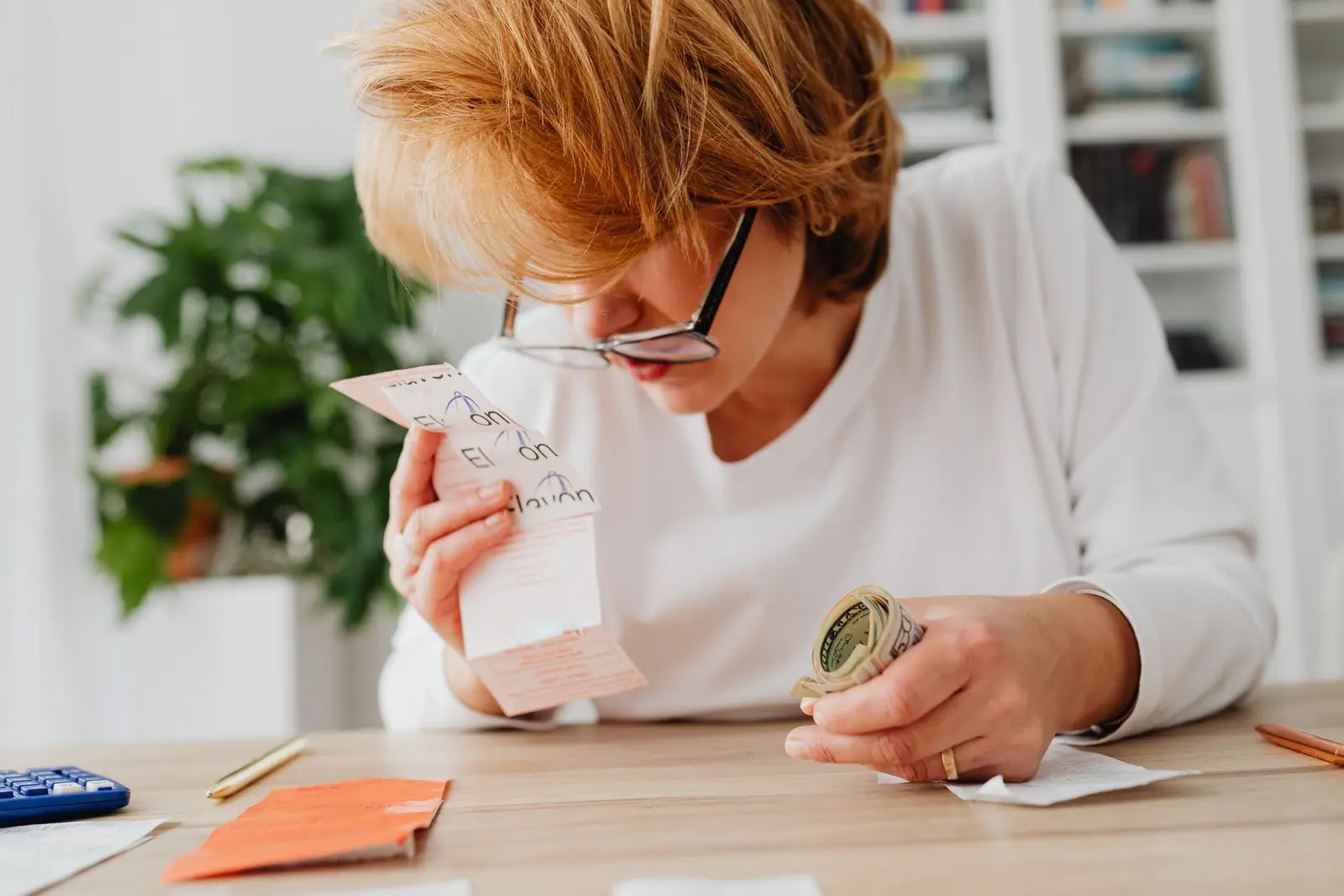 A person wearing glasses looking closely at a paper receipt at a table